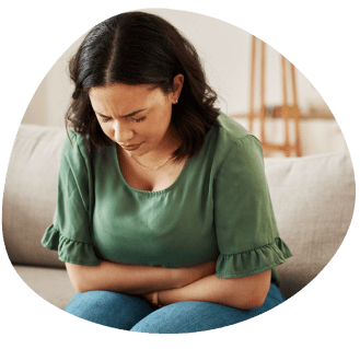 An image of a woman leaning over holding her stomach and frowning with her eyes closed.