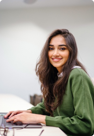 A woman smiling, working on a laptop.